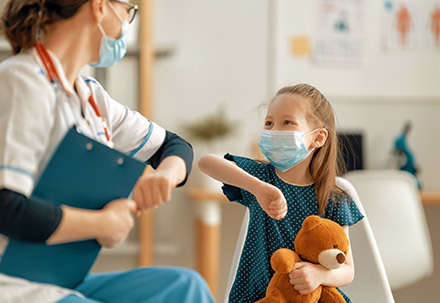 Une médecin et une enfant masquées se disent bonjour avec le coude.